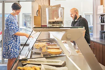 Ein Mann bedient eine Kundin an der Kuchentheke beim Lieblingsgrieche.