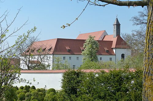 Blick auf den Gebäudekomplex des Klosters in Wemding. Im Vordergrund grüne Büsche und Bäume.
