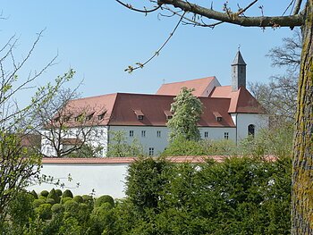 Blick auf den Gebäudekomplex des Klosters in Wemding. Im Vordergrund grüne Büsche und Bäume.
