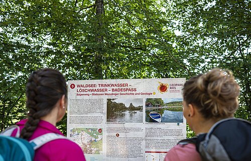 Zwei Freundinnen lesen die Informationstafel "Sagenweg" am Waldsee.