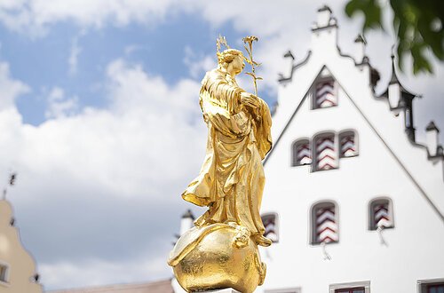 Die goldene Marien Statue vom Marienbrunnen am historischen Marktplatz ist im Vordergrund des Fotos.