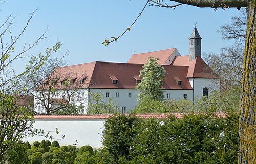 Blick auf den Gebäudekomplex des Klosters in Wemding. Im Vordergrund grüne Büsche und Bäume.