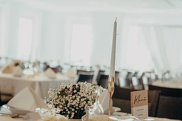 Blick auf einen in hellen Farben gedeckten Tisch mit Gläsern, Blumenvase und Kerze.